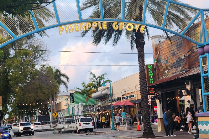 Delray Beach - Dixon Law Firm Arched entrance reading 'Pineapple Grove' over a palm-lined street with shops and pedestrians.