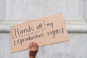 Reproductive Rights Attorney South Florida - Dixon Law Firm A hand holds a cardboard sign that reads,'Hands off my reproductive rights!' in black marker, proclaiming a protest message.